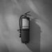 Black and white image of a fire extinguisher hung up on a plain white wall.