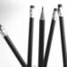 A pointy, sharpened pencil pointing up with four pencils in the background pointing down