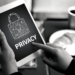 A black and white image of white hand holding an iPad with a padlock icon on the screen and the word privacy below it